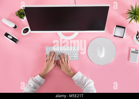 Businessperson Hands On Keyboard Over The Pink Desk At Workplace Stock Photo