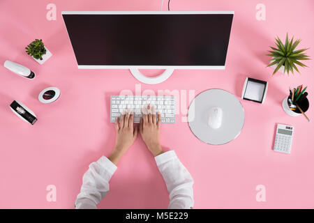 Businessperson Hands On Keyboard Over The Pink Desk At Workplace Stock Photo