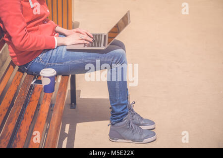 Female hands on laptop keyboard. She is sitting on bench outdoors. Coffee to go next to her. Technology and modern lifestyle concepts. Stock Photo