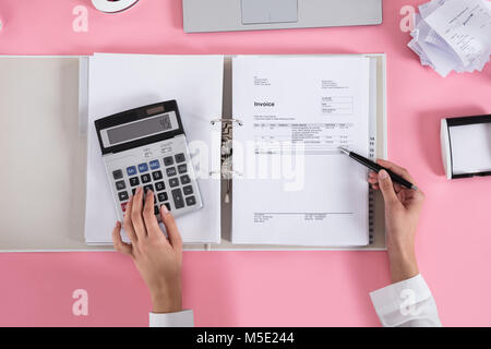 Close-up Of A Businesswoman Using Calculator While Calculating Invoice On Pink Desk Stock Photo