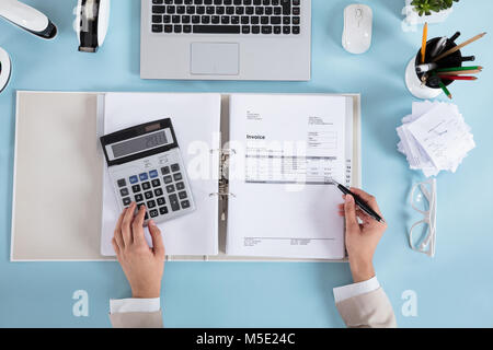 Elevated View Of A Businesswoman Calculating Invoices Using Calculator On Desk Stock Photo