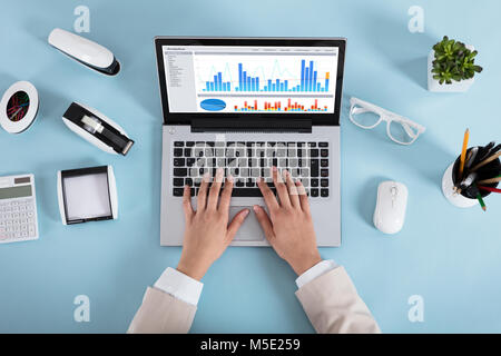 Close-up Of A Businesswoman Analyzing Various Graphs On Laptop On Blue Desk In Office Stock Photo