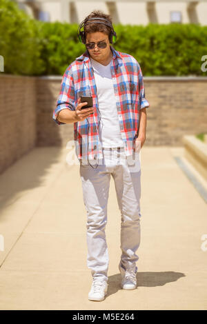 Modern fashionable man looking at smartphone and using music player app to listen his favorite songs with headphones Stock Photo