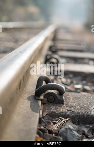 Arty close up of metal fastening system on a railway track. Sharp focus on heavy-duty, forged steel rail clip: fastener ties rail to concrete sleeper Stock Photo