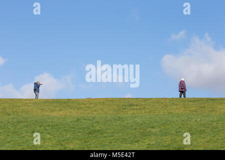 Retired, married couple on grassy hill, out together on bright cold morning taking photographs of each other, practising their photography skills. Stock Photo