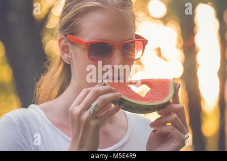 Portrait of young pretty female holding and eating watermelon slice with heart shape in nature. Summertime and lifestyle concepts. Stock Photo