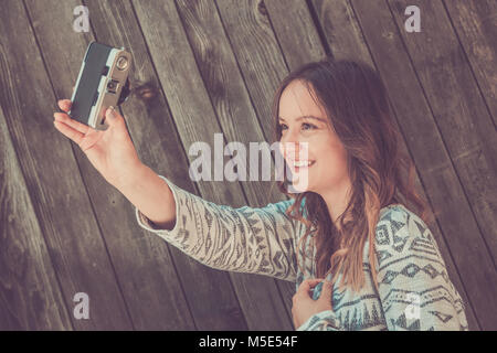 Portrait of young beautiful female taking self portrait by using retro vintage film camera against wooden background Stock Photo
