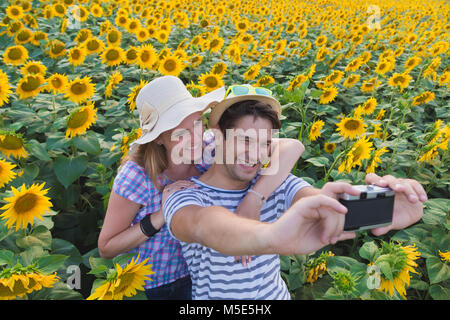 Young heterosexual couple taking selfie in sunflower field by using retro vintage film camera. Love and summertime concepts. Stock Photo