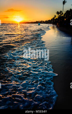 sunrise on the ocean, white sea foam, reflection in the water, shiny sand and silhouettes of palm trees along the morning beach, lonely figures of peo Stock Photo