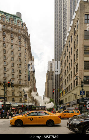 New York, NY, USA - June 06, 2015:Steam coming out of Greeley Square and the intersection West 32 in Manhattan in the spring. Traffic of cars and crow Stock Photo