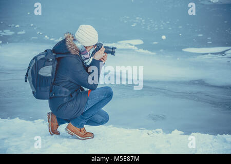 Portrait of female photographer shooting winter landscape next to the frozen lake. Stock Photo