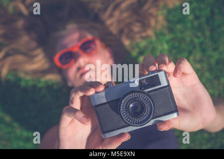 High angle close up view of female lying on field and taking photo by using vintage retro camera Stock Photo