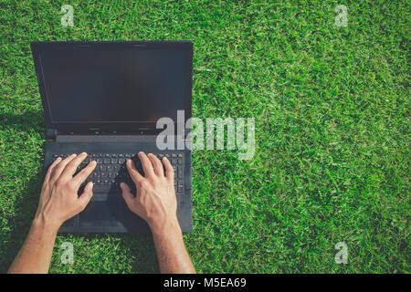 High angle view of man using blank screen laptop on grass. Technology and green energy concepts. Space for copy. Stock Photo