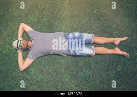 Top down view of man in hat and sunglasses lying in the grass Stock Photo