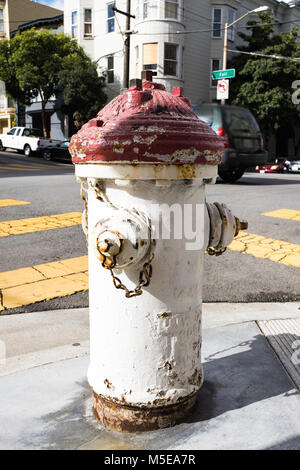 An old vintage fire water hydrant painted white and red on the corner of the street, casting a shadow on a sunny day Stock Photo