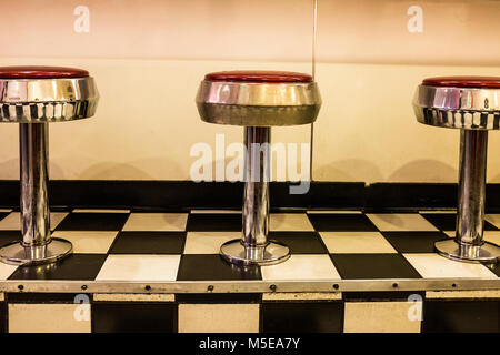 Close up of 50s diner chrome and red stools on black and white checkerboard tiled floor Stock Photo