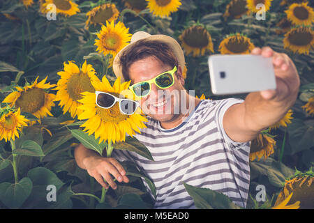 Young man taking selfie with sunflower by using smartphone. Both wearing sunglasses. Summertime concept. Stock Photo