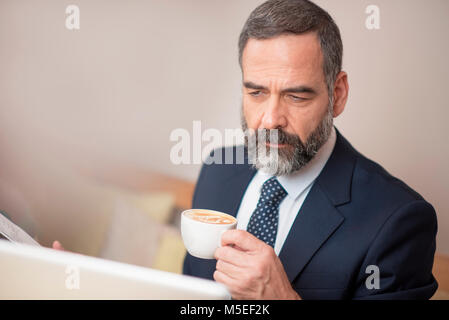 Senior mature business man having a coffee in a coffee shop and working on his computer Stock Photo
