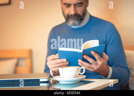 Senior old man reading a book in a coffee shop, enjoying his literary hobby Stock Photo