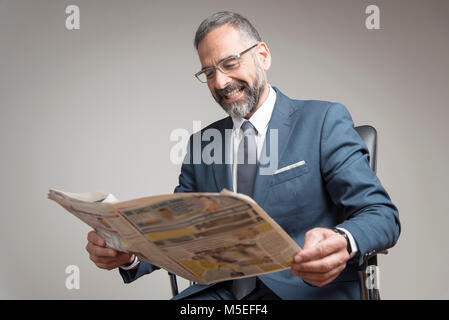 Happy senior business man reading newspaper, amused with its content Stock Photo