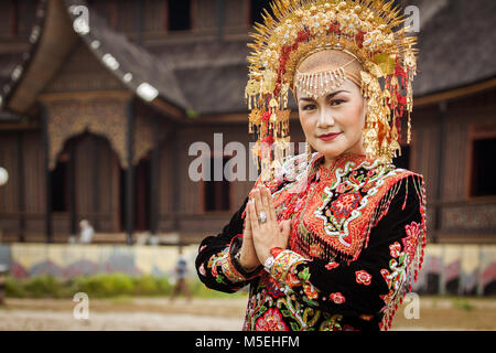 Minangkabau woman portrait dressed in traditional royal clothes with tribal designs and headdress, hands in prayer with Pagaruyung tourist attraction Stock Photo