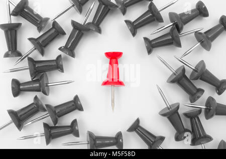 Single red plastic push pin surrounded by scattered gray push pins on white background Stock Photo