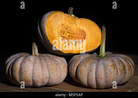Still life image of a half cut orange pumpkin sitting on top of two whole fresh pumpkins isolated on black background. Rustic food and drink photo Stock Photo