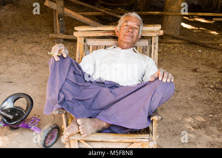 Bagan, Myanmar, December 27, 2017:  Senior man recovers in an armchair and smokes a cigarette Stock Photo