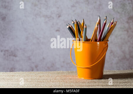 A set of colored pencils on a toy bucket in a beautiful brownish background Stock Photo