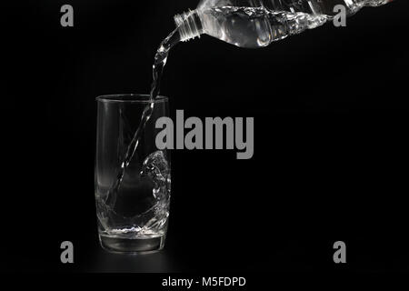 water is poured from plastic bottle into glass isolated on black Stock Photo