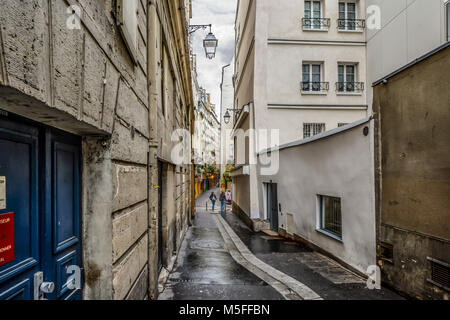 Two young ladies on an early morning walk in the Latin Quarter of Paris France pass through a narrow back alley on a cloudy day. Stock Photo