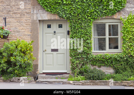 Wooden doors to a charming lime stone cottage surrounded by climbing ivy plant and shrubs . Stock Photo