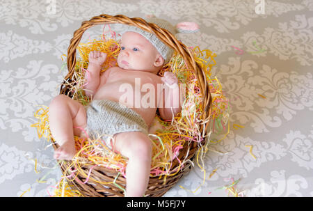 newborn baby girl laying in Easter basket wearing handmade knit bunny outfit Stock Photo