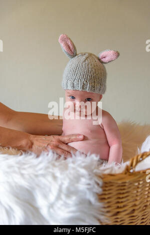 baby in homemade knit bunny ear hat sitting in Easter basket with funny facial expression Stock Photo
