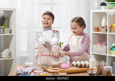 Girl and boy cooking in home kitchen. Children show hands with flour. Stock Photo