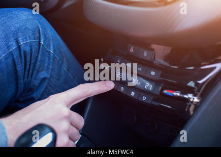 Changing the temperature on the air conditioner in the car. Hand touch the climate control device. Stock Photo