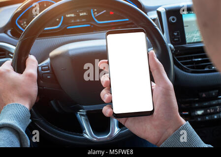 Man holding smartphone in car with isolated, white display for mockup, app, or web site design promotion. Modern car interior in background. Stock Photo