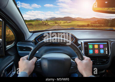 Driving car using the smart technologies that are displayed on board display. View from the driver's sight on the steering wheel, road and interior. Stock Photo