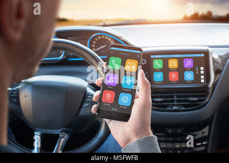 Driver uses a mobile phone with smart driving assistance apps. The app is connected to a car computer and is displayed on the board display. Stock Photo