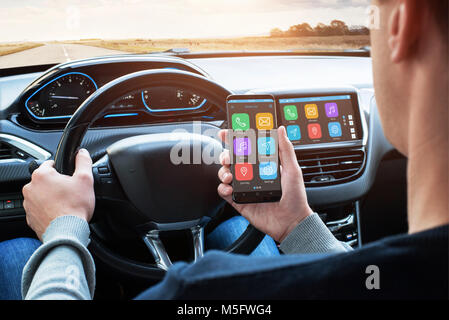 Car driver use smart phone with smart car app and use connection with car infotainment system while driving. Stock Photo