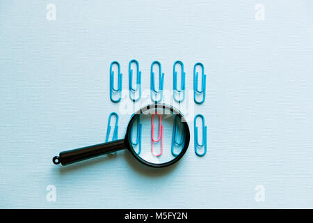a magnifying glass and paper clips on a blue background. Stock Photo