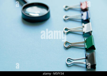 a magnifying glass and colored paper clips on a blue background Stock Photo