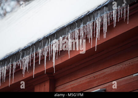 Detail of icicles hanging from snow covered roof on red wooden building Stock Photo