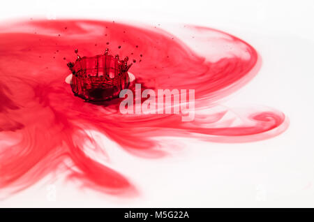 Creative photography image of what is known in water drop photography as a water splash crown. A red colored droplet of water on impact with a surface Stock Photo