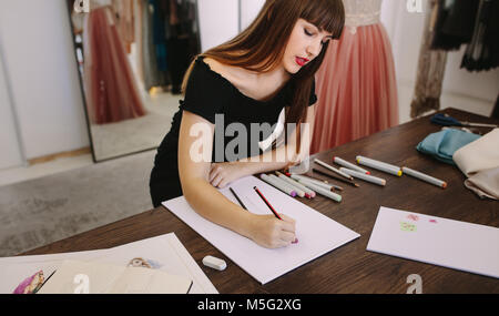 Female fashion entrepreneur sketching a design sitting at her table. Fashion designer making a drawing in her cloth shop.