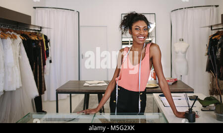 Female fashion designer standing at her desk in her boutique. Female dress designer in her cloth shop with a measuring tape around her neck. Stock Photo