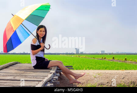 asian woman with umbrella sitting on a bridge and a paddy field of Sekinchan behind Stock Photo