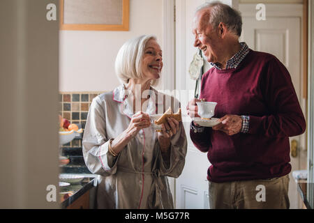 Senior couple are enjoying breakfast and talking  in the kitchen. They are both drinking tea. Stock Photo