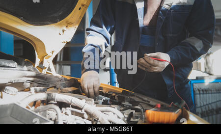 Mechanic in car workshop works with car electrics - electrical wiring, voltmeter - small business Stock Photo