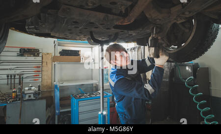 Mechanic unscrewing parts of automobile's bottom under lifted car Stock Photo